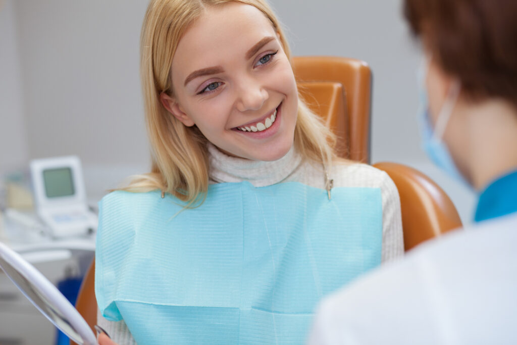 Young cheerful blond haired woman smiling joyfully during medical consultation with her dentist.