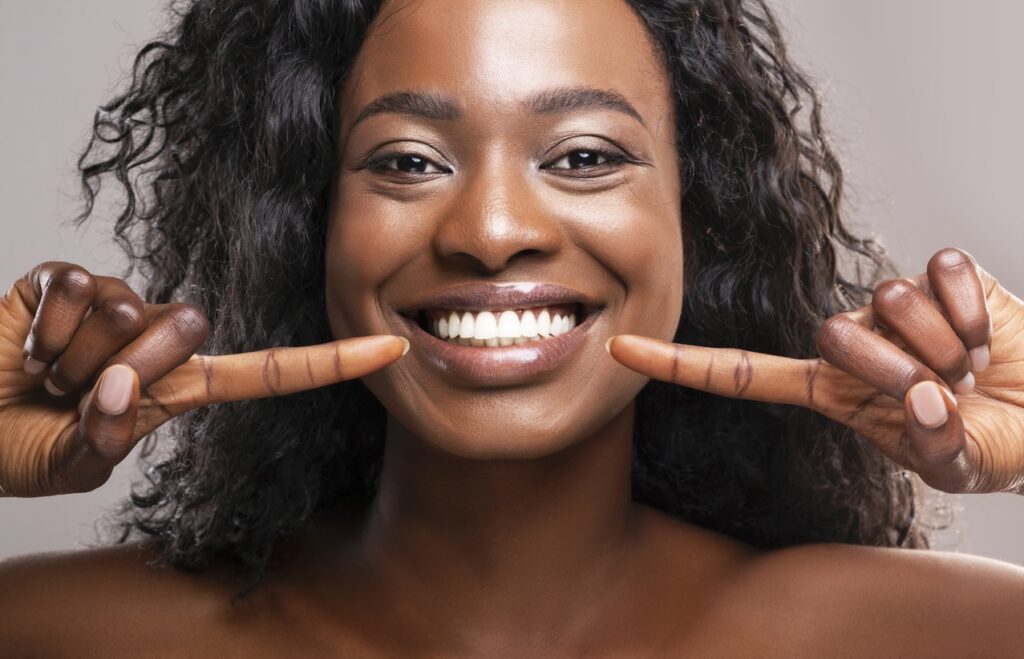 Gorgeous woman with a full makeover pointing at her stunning smile with both hands