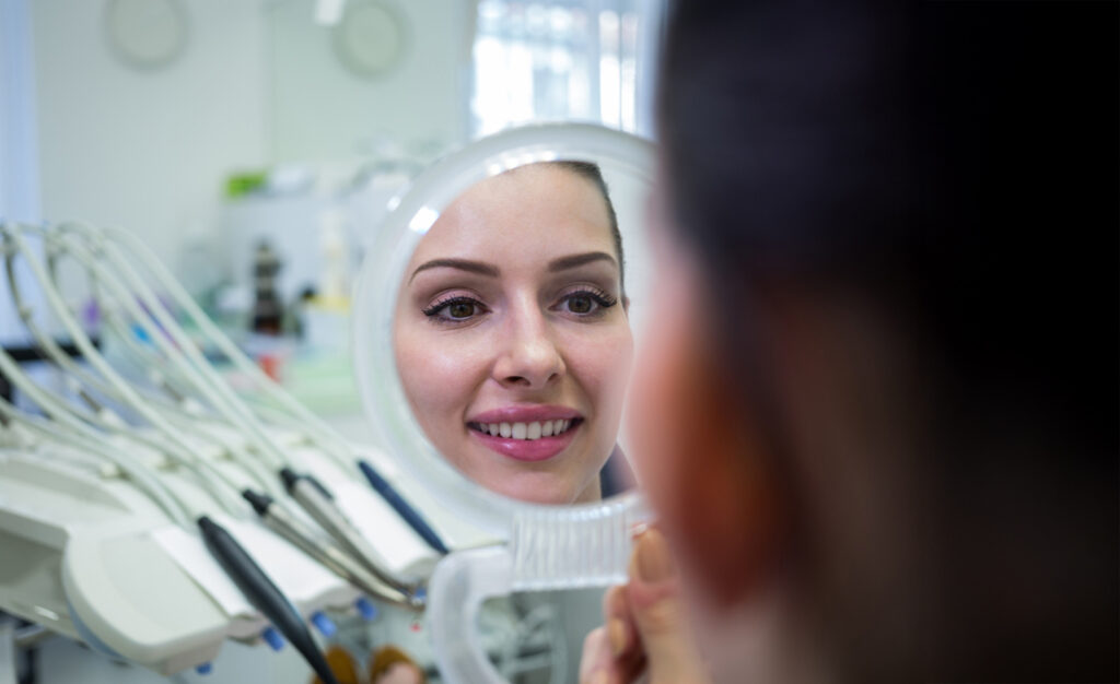 Woman examining her smile in a mirror at her dentist’s office