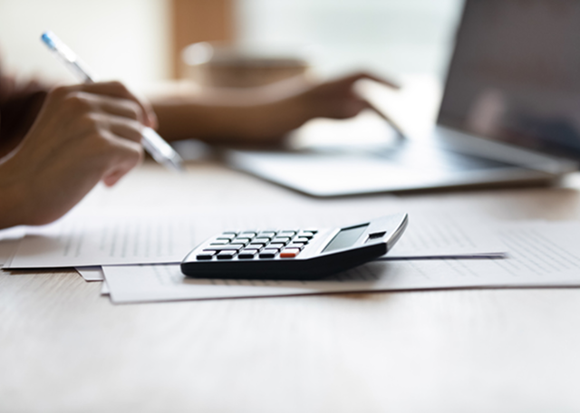 Close up of a calculator with the hands of a woman typing with one hand and holding a pen in the other