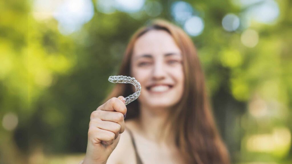 Woman holding her Invisalign aligner outside on a warm spring day