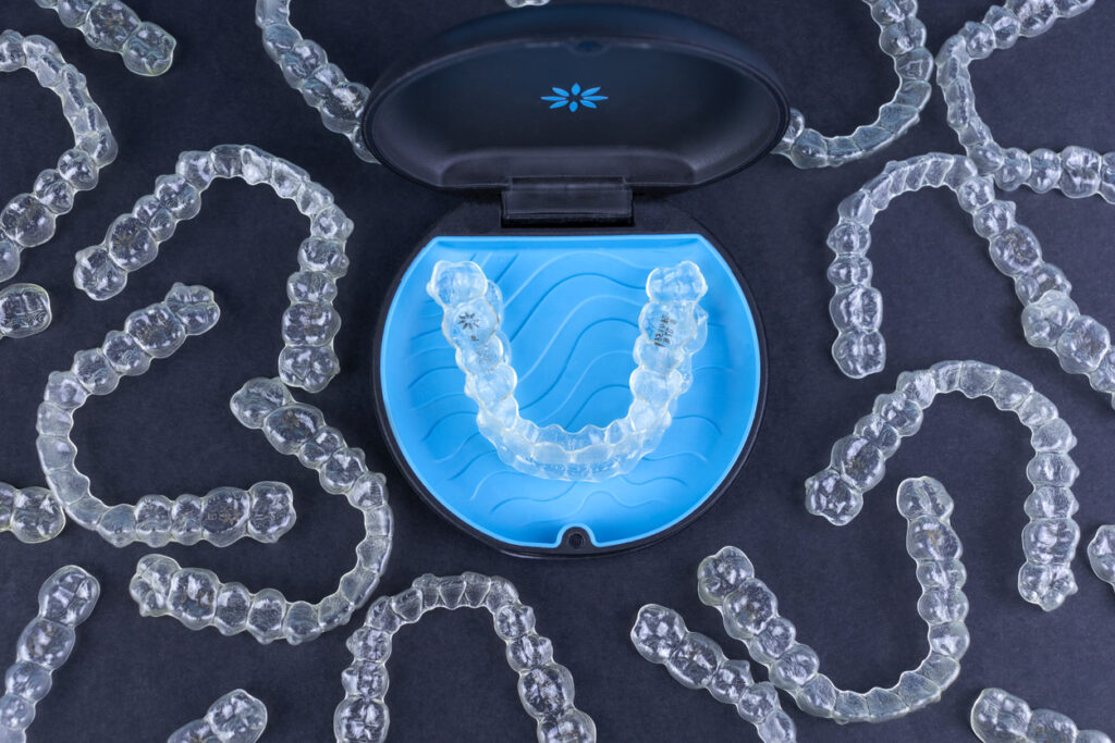 Invisalign® aligners in a blue Invisalign case with many invisalign aligners scattered around