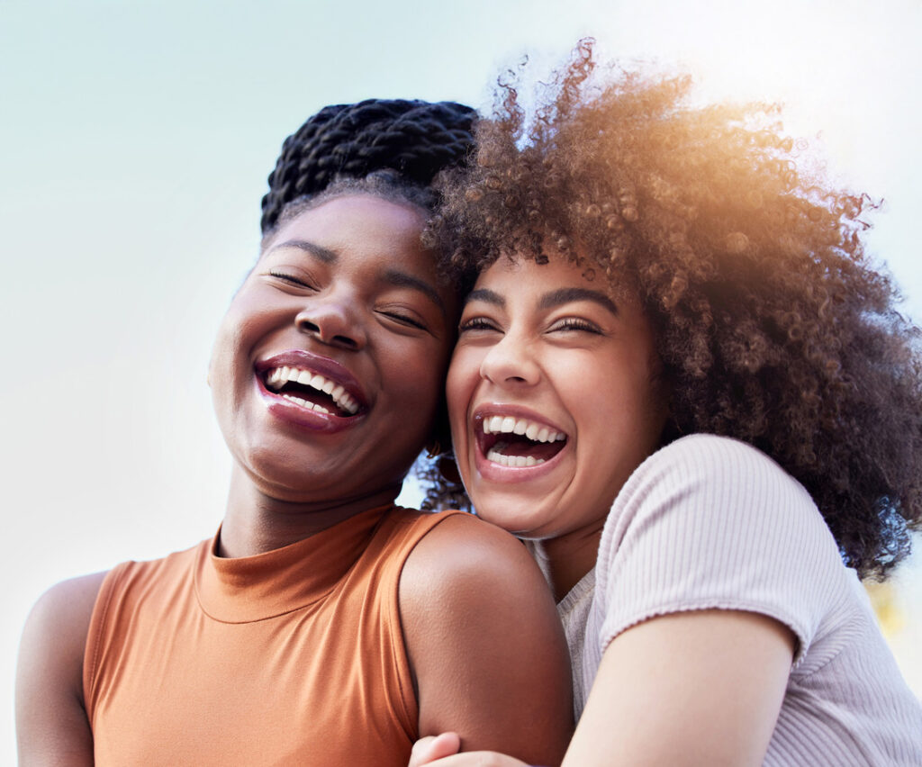 Two woman with beautiful smiles embracing in the summer sun