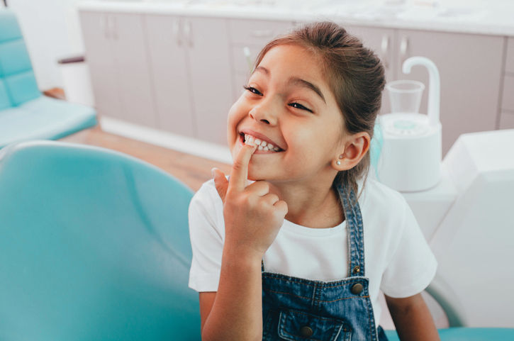 Small child smiling and pointing to her top front teeth while a dental assistant collects her history